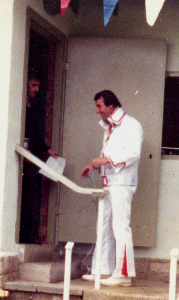 Denis Fletcher dressed as Elvis in a white suit with red trim, at the clubhouse door
