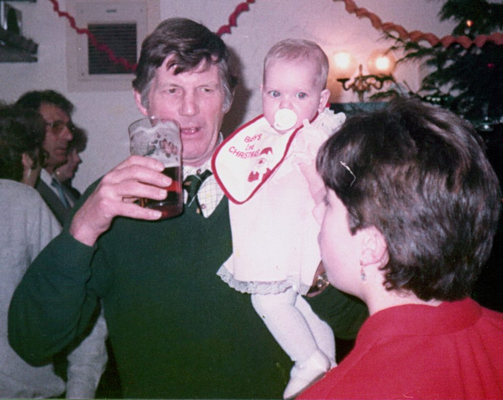 Jim Moulton raising a pint while holding a baby in a Baby's 1st Christmas bib